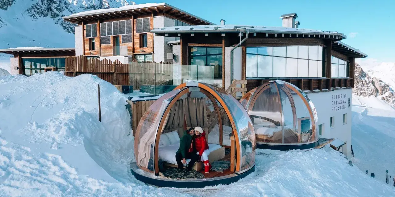 Coppia in una bolla trasparente innevata, perfetta idea su dove andare a gennaio in Italia per un soggiorno da sogno tra le montagne.