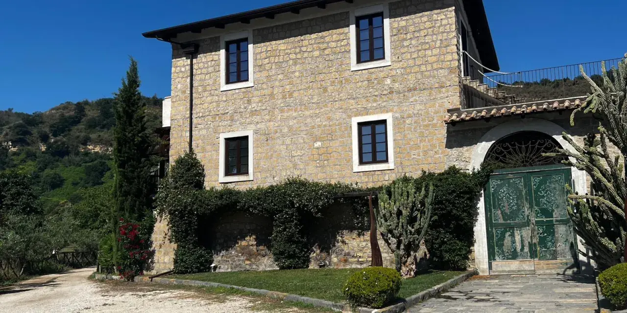 La Masseria del Carmine Maggiore, con le sue mura in pietra chiara e il verde rigoglioso, incanta sotto un cielo azzurro.