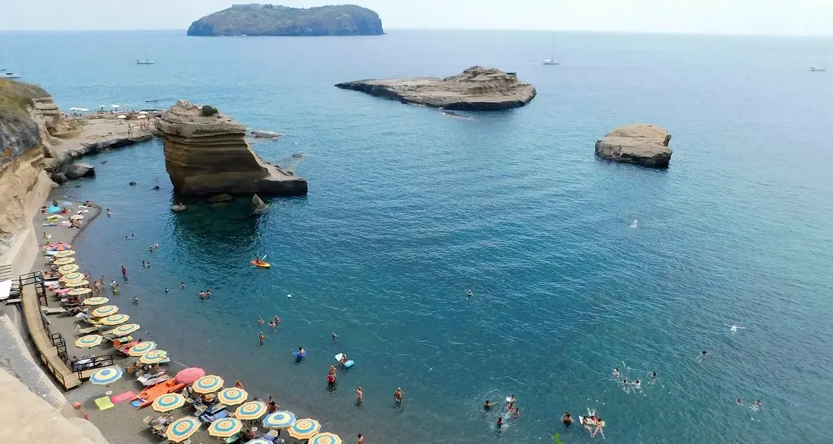 Le **spiagge** di Ventotene, con ombrelloni colorati e bagnanti in un mare azzurro, fanno da cornice a scogli suggestivi e all'isola di Santo Stefano in lontananza.