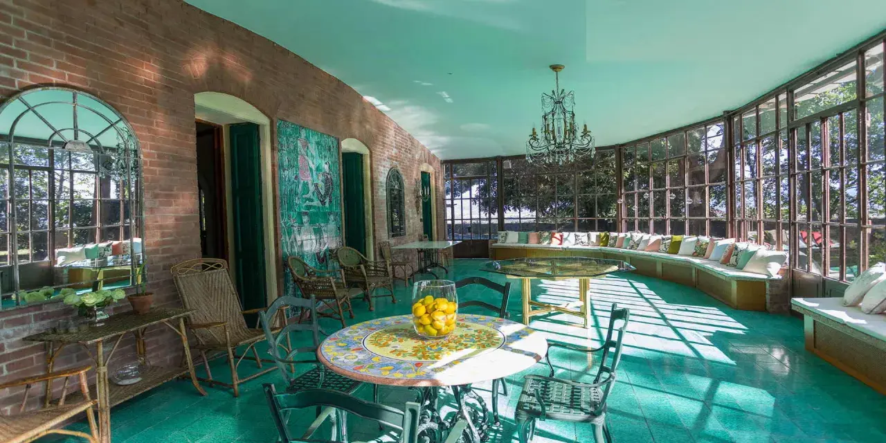 Veranda luminosa della villa dei cipressi a Sona, con pavimenti verdi, mobili in vimini e un grande divano curvo con cuscini colorati.
