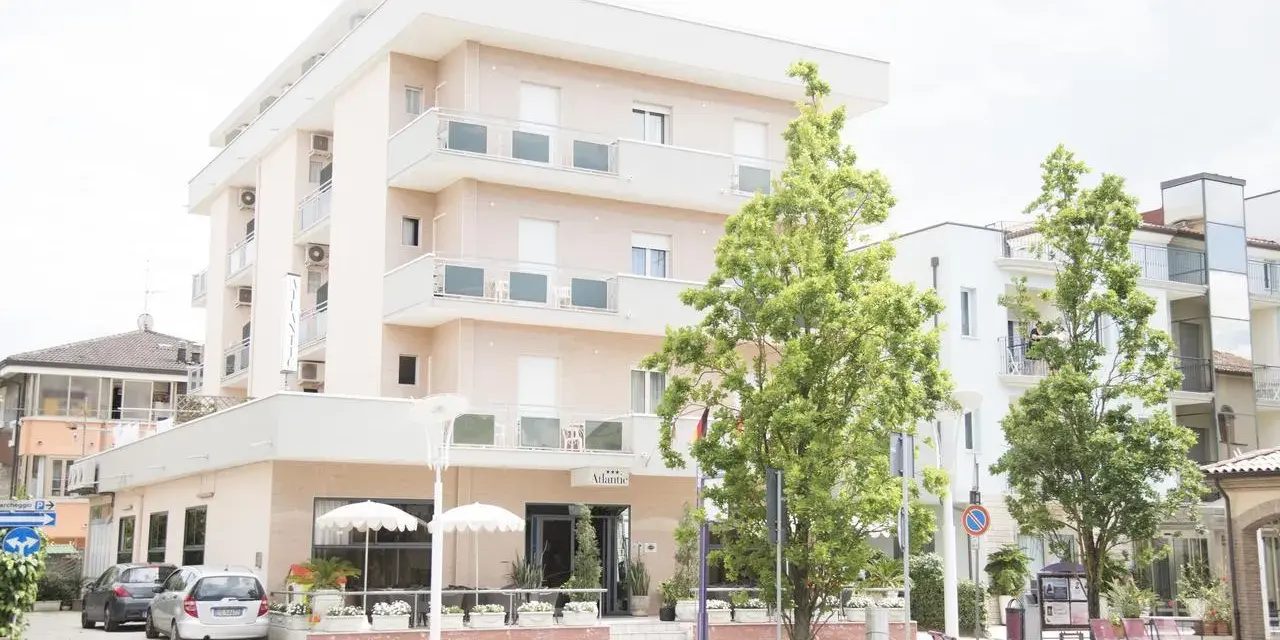 Hotel Atlantic Igea Marina: scopri i prezzi per la tua vacanza al mare. Edificio moderno con alberi verdi davanti.