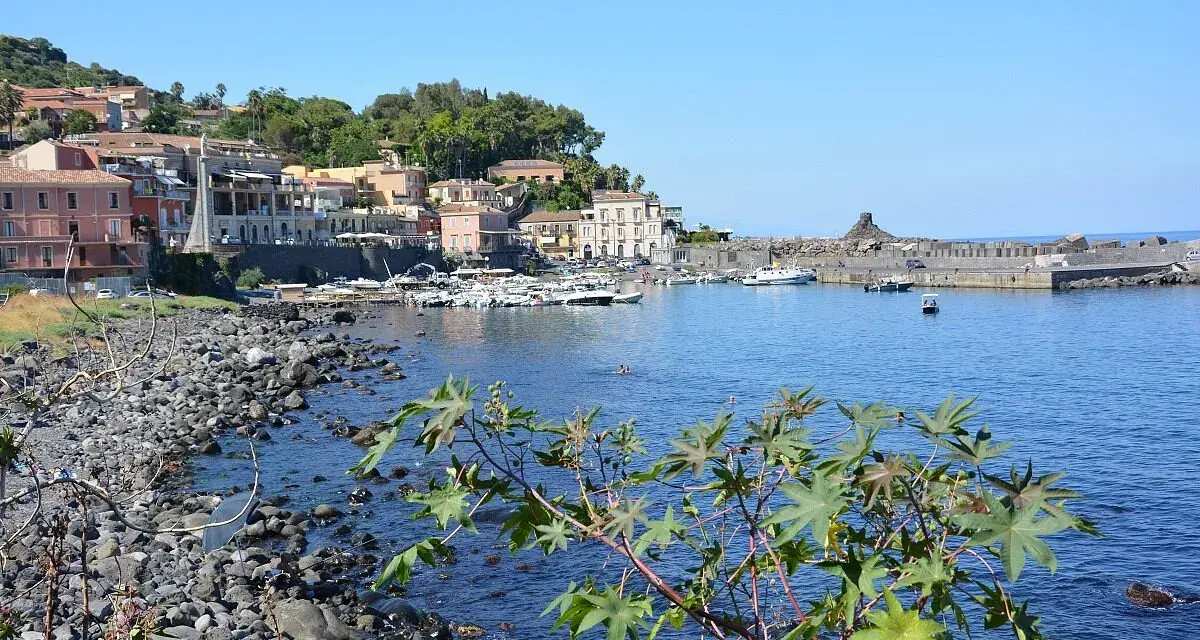 Il lungomare di Acireale, con case colorate, barche ormeggiate e il mare azzurro.