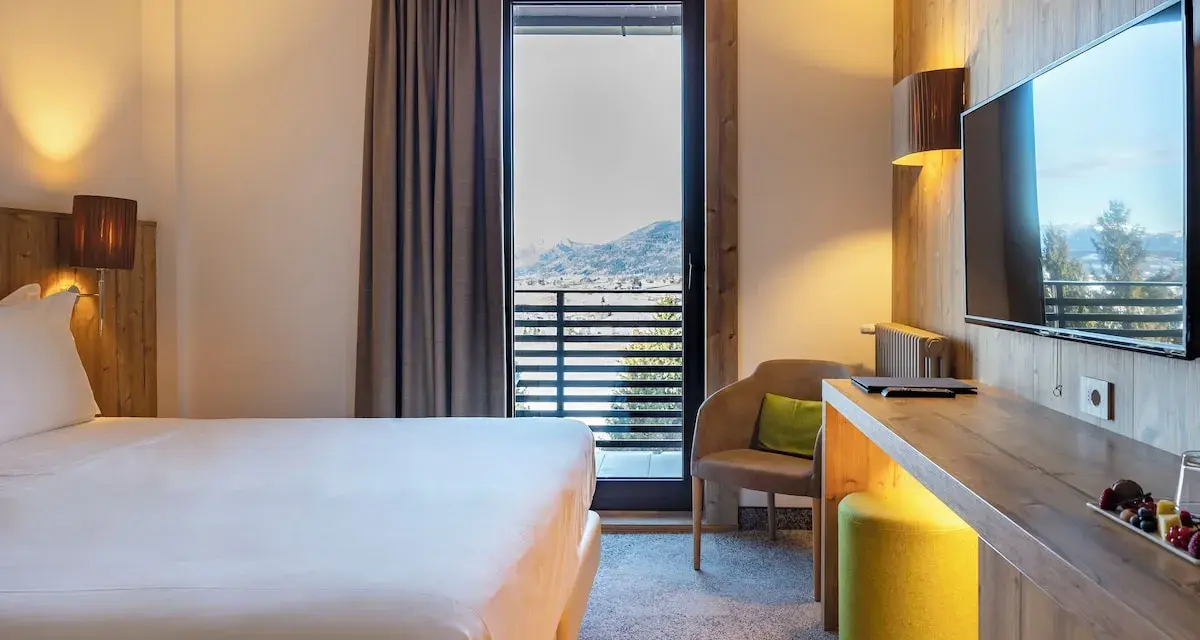 Camera accogliente con vista panoramica, tipica del Linta Hotel Asiago. Letto comodo, poltrona e balcone con paesaggio montano.