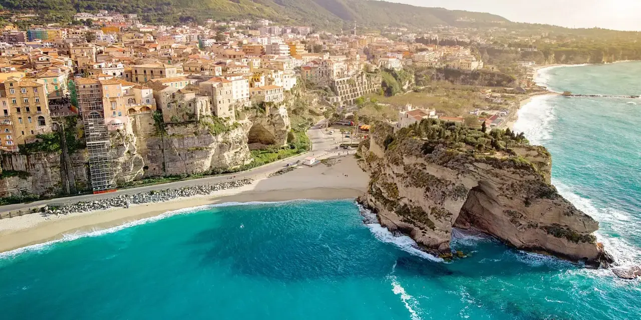 Panoramica mozzafiato delle **calabrie spiagge** con case colorate aggrappate alle scogliere e un mare turchese.