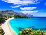 Una baia incantevole con acque cristalline e sabbia dorata, tra le spiagge più belle in Sicilia. Montagne verdi sullo sfondo.
