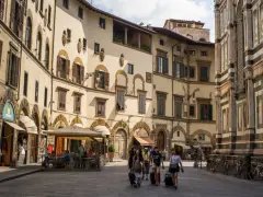 Un gruppo di turisti con valigie a rotelle cammina in una piazza fiorentina, un'immagine perfetta per un **viaggio in Toscana**.