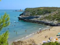 Splendida spiaggia di Peschici con gente che si gode il sole e il mare cristallino, incorniciata da una scogliera verdeggiante.