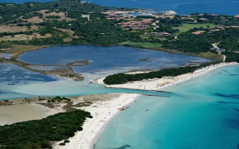 Vista aerea della spiaggia La Cinta con acque turchesi, lagune interne e vegetazione lussureggiante.