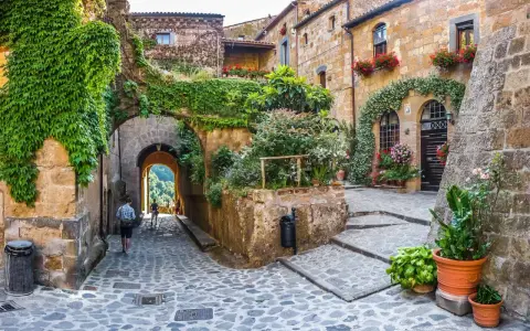 Un vicolo acciottolato tra antiche case in pietra, ricoperte di edera e fiori. Un invito a scoprire i borghi da visitare nelle Marche.