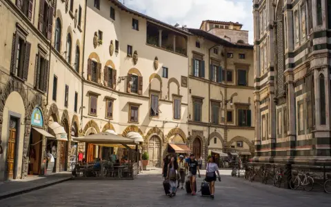 Un gruppo di turisti con valigie a rotelle cammina in una piazza fiorentina, un'immagine perfetta per un **viaggio in Toscana**.
