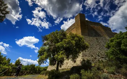Roccia imponente e cielo azzurro con nuvole bianche: ecco cosa vedere a Pomarance, con un escursionista che ammira la fortezza.