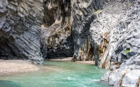 Acque cristalline scorrono tra le imponenti pareti basaltiche delle gole dell'Alcantara, creando una spiaggia naturale suggestiva.