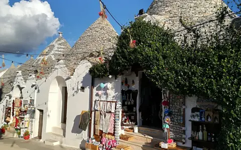 Trulli caratteristici della Valle d'Itria cosa vedere: negozi di souvenir con prodotti locali e decorazioni tipiche sotto un cielo azzurro.