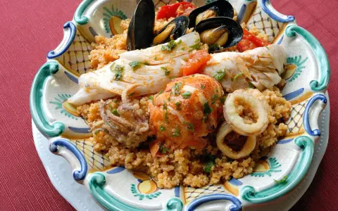 Piatto di pesce misto con couscous: ecco cosa mangiare a Trapani. Gamberi, calamari, pesce bianco e cozze.