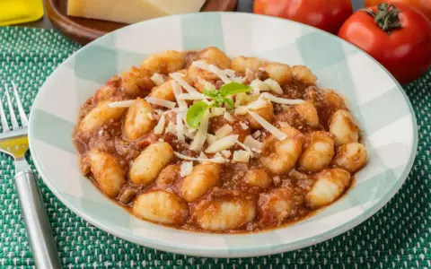 Gnocchi al ragù, un classico tra i piatti tipici di Perugia, serviti con parmigiano grattugiato e basilico fresco.