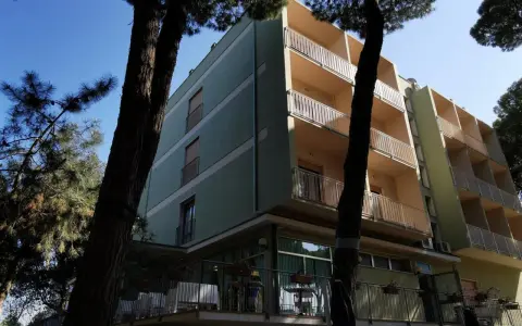 Edificio del pine beach hotel rosolina mare, con balconi e alberi di pino davanti.