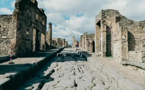 Antica strada romana a Pompei, con rovine di edifici e turisti che passeggiano. Un'ottima guida per come visitare Pompei.