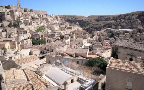 Panoramica dei Sassi di Matera, un **itinerario** suggestivo tra antiche case scavate nella roccia e tetti in cotto sotto un cielo azzurro.