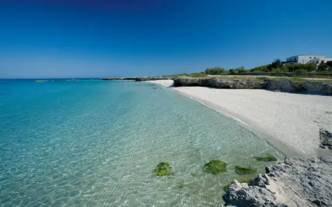 Spiaggia bianca e mare cristallino in Puglia, con rocce e vegetazione. Un angolo di paradiso per godersi il sole e il **mare** della **Puglia**.