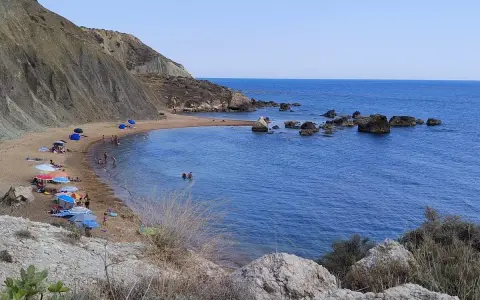 Spiaggia di Cala Vincenzina con scogliere, ombrelloni colorati e bagnanti che si godono il mare azzurro.