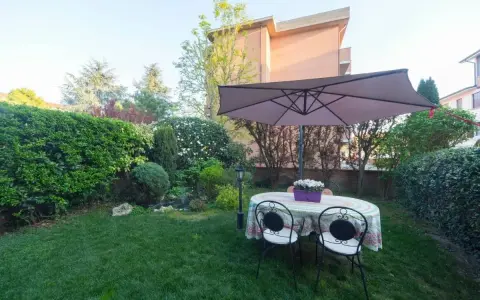 Un giardino curato con tavolo, sedie e ombrellone, circondato da siepi e alberi. Sembra l'albero dei gufi, un luogo magico per rilassarsi.