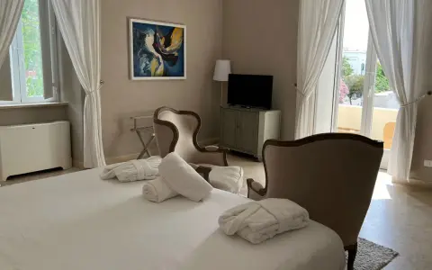 Camera accogliente al relais Corte degli Aragonesi, con letto, accappatoi, poltrone e vista su un balcone fiorito.