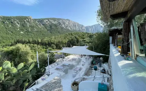 Terrazza panoramica con vista sui monti di Oliena, Sardegna. Arredamento bianco, cactus e vegetazione rigogliosa.