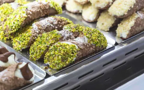 Cannoli siciliani, dolci tipici siciliani, ricoperti di pistacchi e zucchero a velo, in una vetrina.