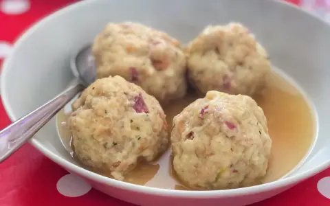Canederli in brodo, un classico dei piatti tipici trentino alto adige, serviti in una ciotola bianca su un tovagliolo rosso a pois bianchi.