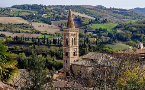 Campanile in borgo marchigiano, tra colline verdi e campi dorati, ideale per itinerari Marche autunnali.