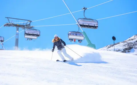 Donna scia su pendio innevato, con seggiovie sullo sfondo. Perfetta per la tua settimana bianca dove andare.