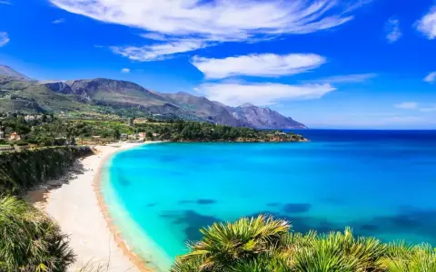 Una baia incantevole con acque cristalline e sabbia dorata, tra le spiagge più belle in Sicilia. Montagne verdi sullo sfondo.