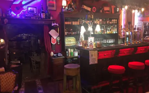Interno della locanda del Principe a Artena, con chitarra elettrica luminosa, bancone bar e sgabelli rossi.
