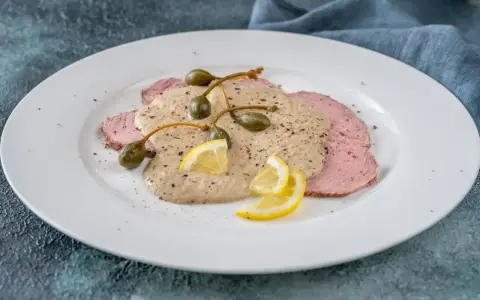Vitello tonnato, uno dei piatti tipici di Torino, con fettine di carne rosa, salsa cremosa, capperi e limone.