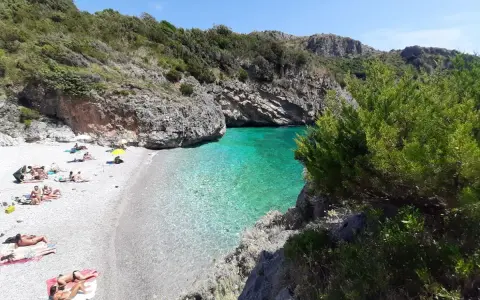 Spiaggia di ciottoli con gente che prende il sole e acque cristalline nel **Cilento mare**.