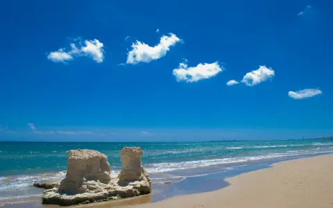 Spiagge bianche in Sicilia, con rocce scolpite dal mare e un cielo azzurro pieno di nuvole bianche.