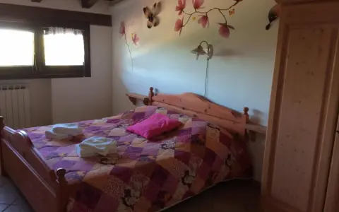 Camera accogliente in un agriturismo al Selvadigo, con letto, coperta colorata, cuscino rosa e decorazioni a farfalle e fiori sul muro.