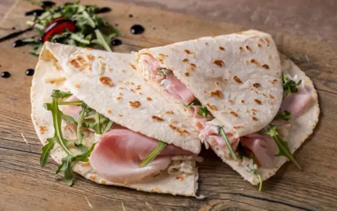 Piadina romagnola con prosciutto, rucola e formaggio. Un classico esempio di cosa si mangia in Emilia Romagna, semplice e gustosa.
