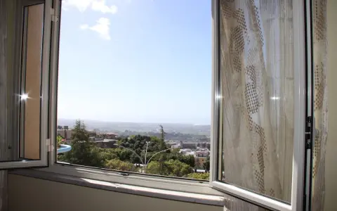 La terrazza sulla valle offre una vista panoramica su un paesaggio collinare con case e alberi verdi sotto un cielo azzurro.