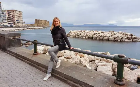 Donna sorridente sul lungomare di Napoli, con Castel dell'Ovo sullo sfondo. Perfetto per scoprire cosa vedere a Napoli in 3 giorni.
