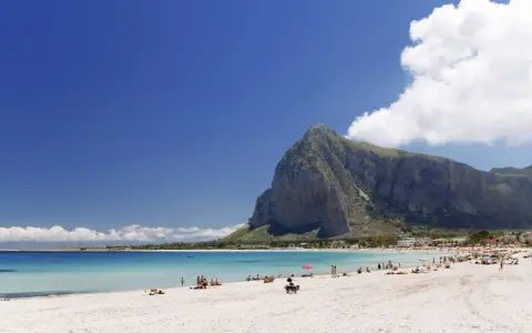 Spiaggia di San Vito Lo Capo, Sicilia, con il Monte Monaco imponente sullo sfondo e il mare cristallino che invita a un bagno.