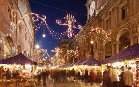 Una strada illuminata da lucine natalizie, con bancarelle e gente che passeggia: ecco i mercatini di Natale più belli.