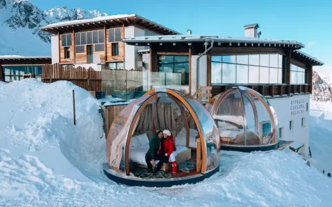 Coppia in una bolla trasparente innevata, perfetta idea su dove andare a gennaio in Italia per un soggiorno da sogno tra le montagne.