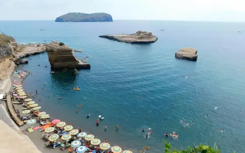 Le **spiagge** di Ventotene, con ombrelloni colorati e bagnanti in un mare azzurro, fanno da cornice a scogli suggestivi e all'isola di Santo Stefano in lontananza.