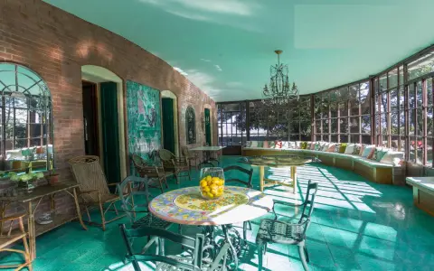 Veranda luminosa della villa dei cipressi a Sona, con pavimenti verdi, mobili in vimini e un grande divano curvo con cuscini colorati.