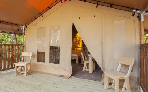 Tenda accogliente nel Luxor Chianti Glamping Village, con sedie in legno sulla veranda e vista sull'interno arredato.