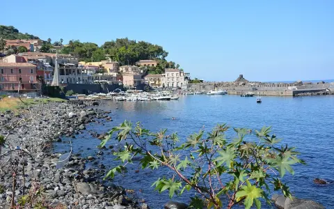 Il lungomare di Acireale, con case colorate, barche ormeggiate e il mare azzurro.