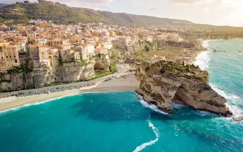 Panoramica mozzafiato delle **calabrie spiagge** con case colorate aggrappate alle scogliere e un mare turchese.