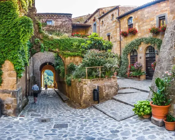 Un vicolo acciottolato tra antiche case in pietra, ricoperte di edera e fiori. Un invito a scoprire i borghi da visitare nelle Marche.