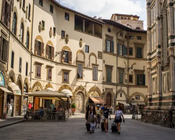 Un gruppo di turisti con valigie a rotelle cammina in una piazza fiorentina, un'immagine perfetta per un **viaggio in Toscana**.